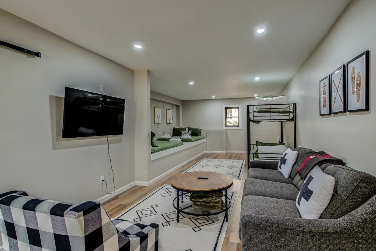 A welcoming lower-level bunk room scene showcasing a bunk bed, comfortable sofa, coffee table, and TV. The room is designed for both sleeping and leisure activities, emphasizing a playful, social vibe perfect for kids and teens.