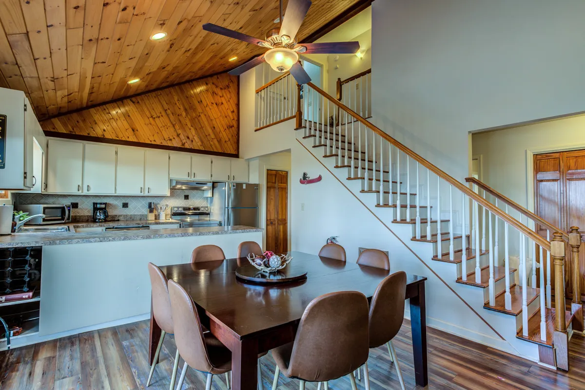 An open dining area featuring a large table, staircase, and kitchen cabinetry, exuding warmth and togetherness. The space is ideal for shared meals, storytelling, and cozy evenings, connecting the comfort of the lodge to the excitement of winter activities.