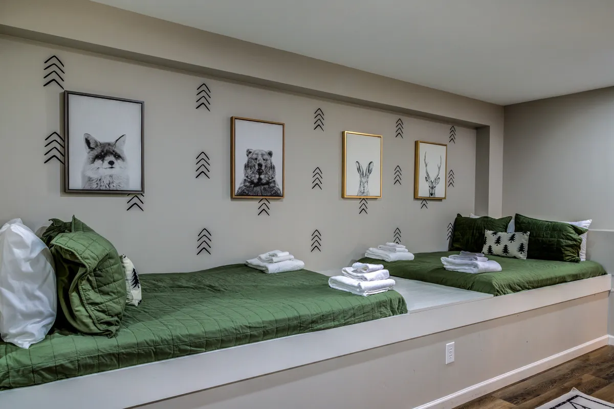 A playful, comfortable bedroom scene featuring green bedding, animal portraits on the wall, and decorative pillows. The setting feels inviting and spirited, ideal for children or families looking to relax after a day of outdoor adventure.