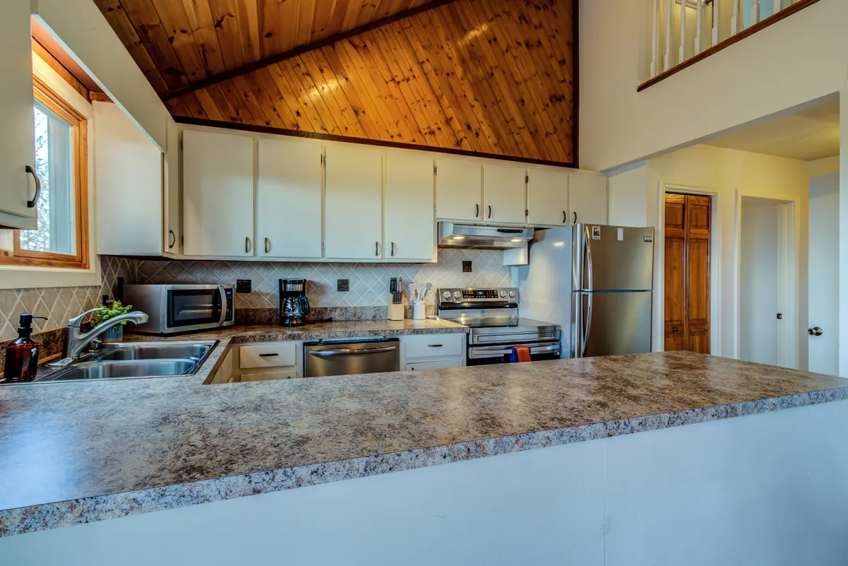 A contemporary kitchen scene with a spacious island, sleek stainless steel appliances, warm wooden ceilings, and plenty of room for socializing or preparing meals. The kitchen is ready for both casual breakfasts and large family feasts.