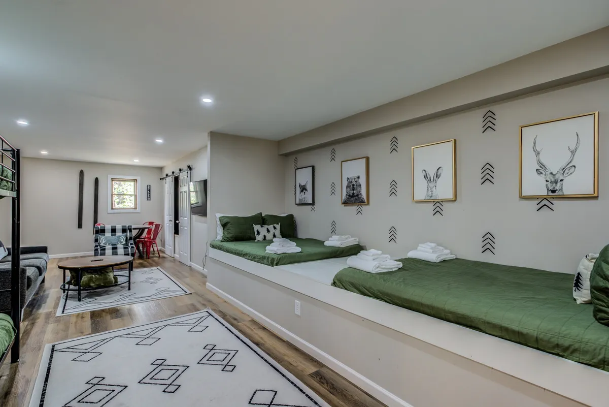 A spacious, inviting living area with green bedding, animal-themed art on the walls, wooden flooring, and a cozy sofa seating area. The room radiates warmth and comfort, making it ideal for both relaxation and socializing after a day outdoors.